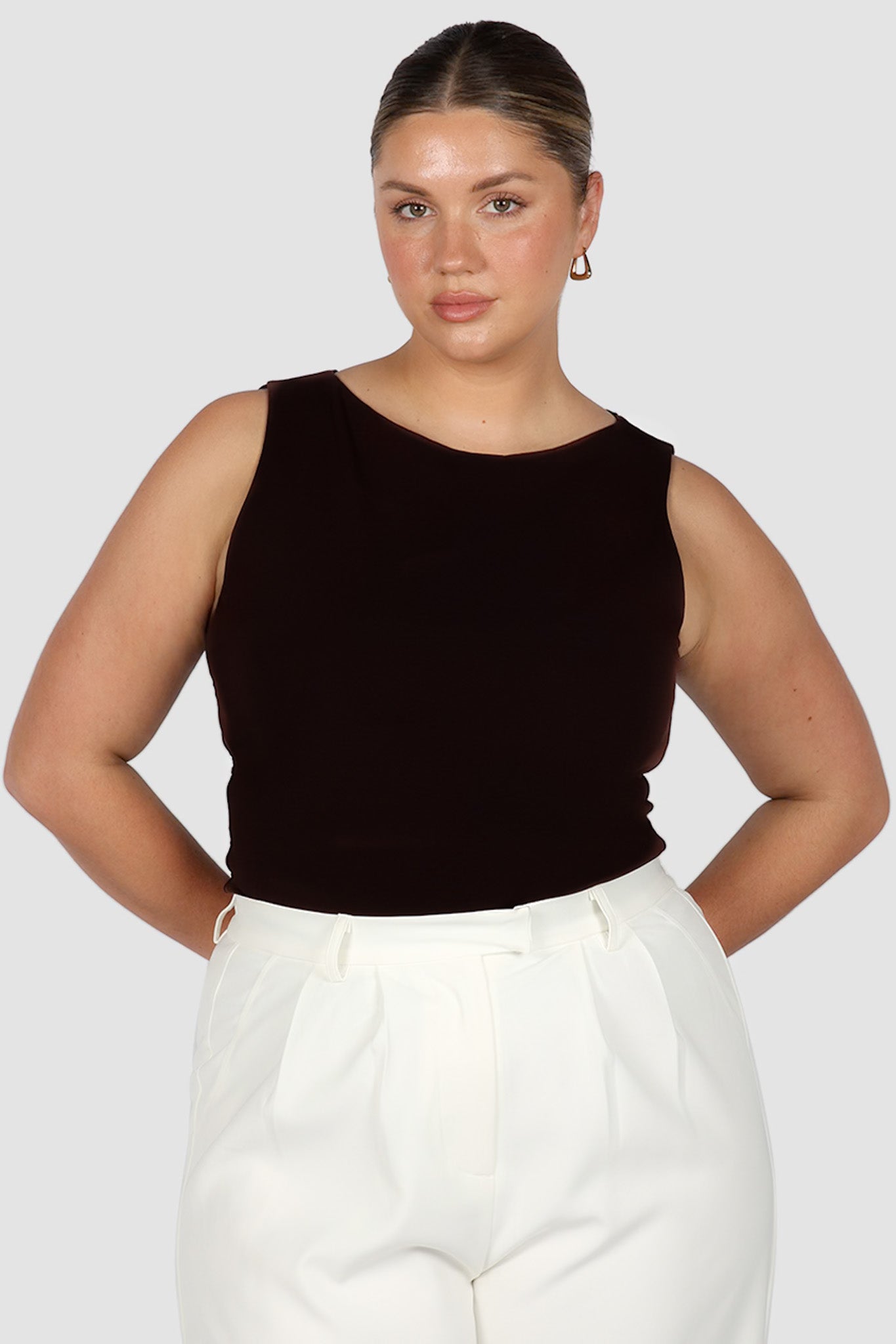 A model wearing a black sleeveless top with a high neck and full coverage back, paired with white pants.