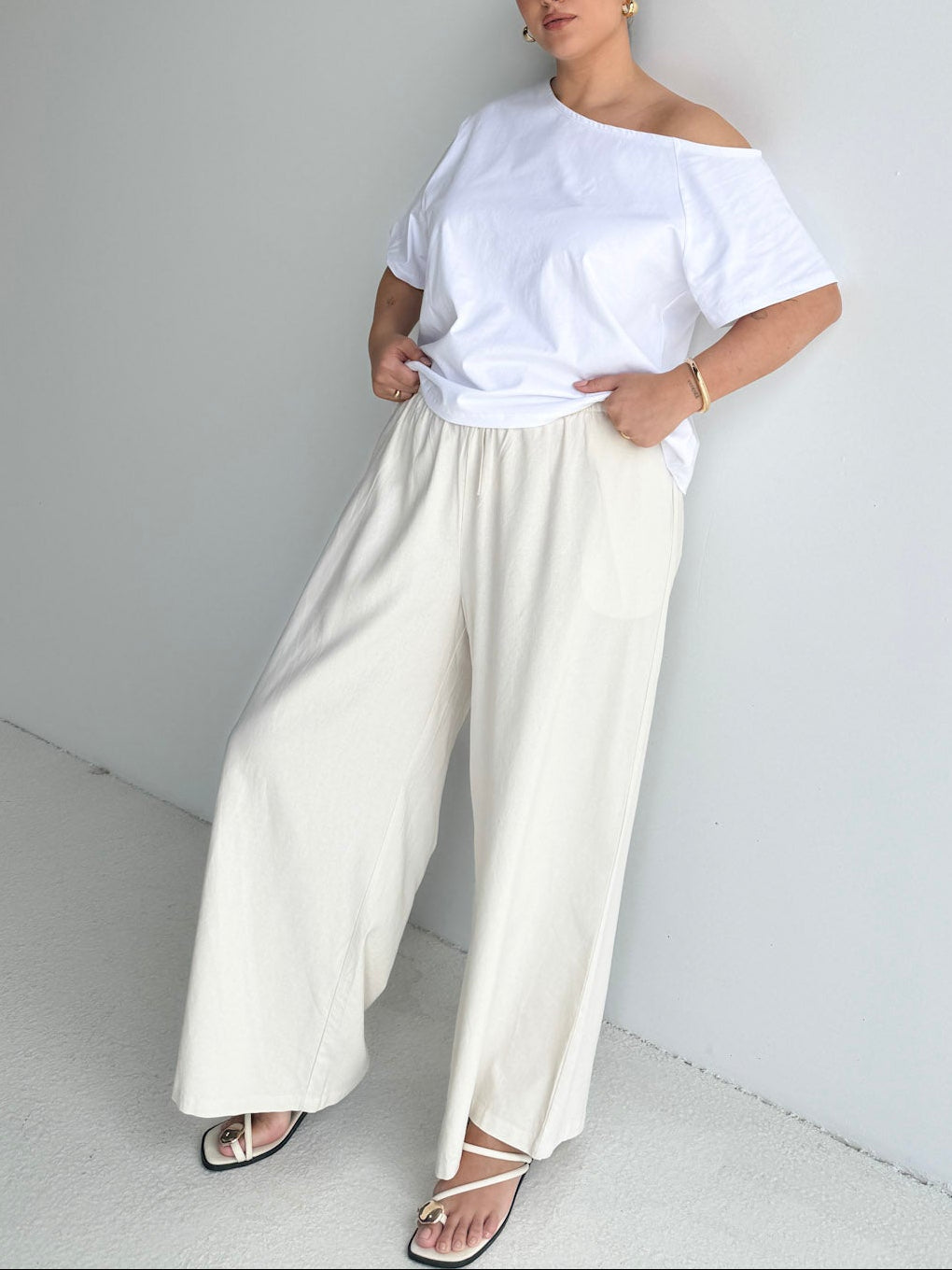 Person wearing a white off-shoulder top and cream wide-leg pants against a plain background