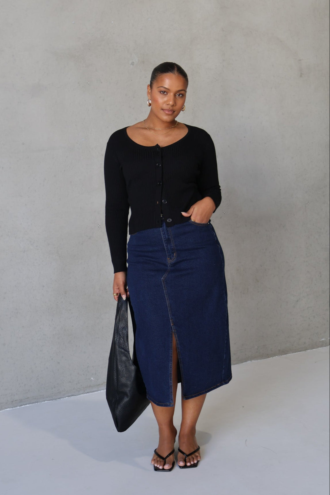 Woman wearing a black top and blue skirt against a plain background